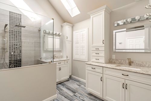 Walk-in shower with mosaic tile accent, white vanity tower and shuttered window