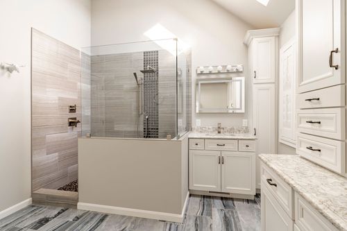 Skylit bathroom with mosaic-tiled walk-in shower and white vanity cabinetry