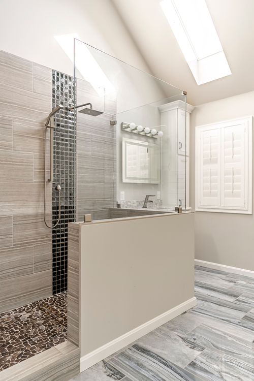 Glass-enclosed shower with mosaic tile column and white linen cabinet