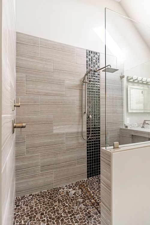 Walk-in tile shower with mosaic accent strip and pebble stone floor