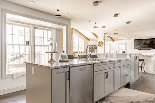 Close-up of a marble kitchen island with gray cabinetry, a glass cake stand and pendant lighting