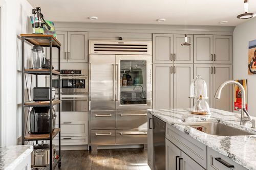 Kitchen with tall stainless built-in refrigerator, gray cabinetry and open metal shelving