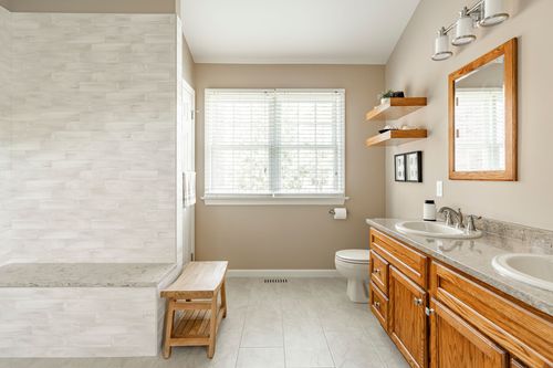 Bathroom with tile shower, teak bench, wood-framed mirror and oak vanity