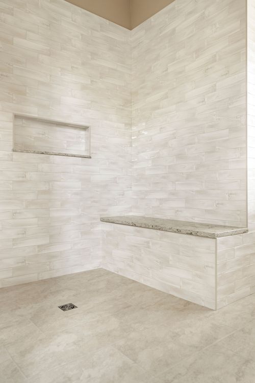 Corner of a tiled walk-in shower with storage niche, bench and drain