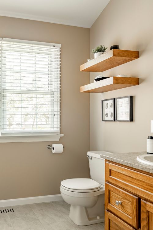 Bathroom with floating wood shelves, framed artwork and oak vanity edge near a toilet