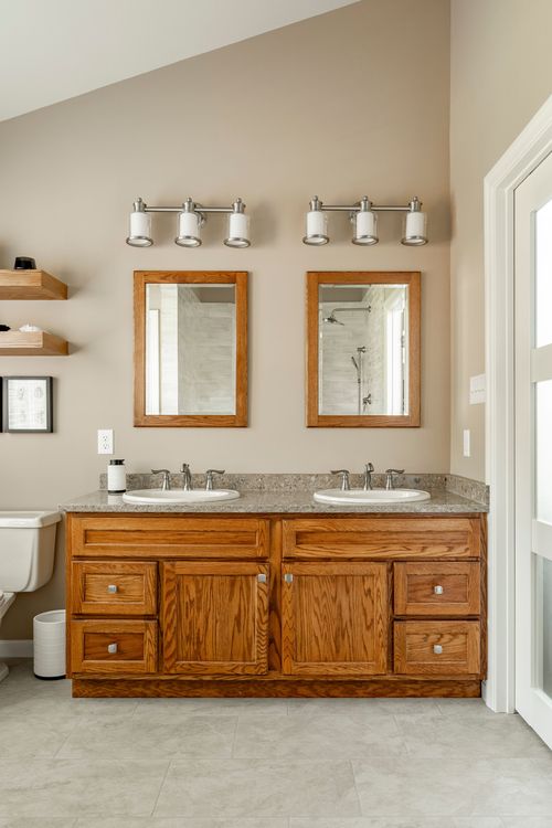 Close view of an oak double vanity with granite counter and framed mirrors