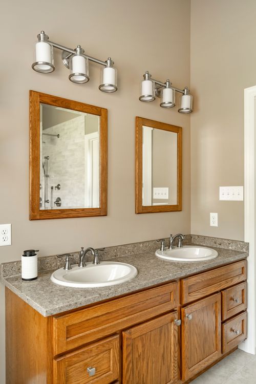 Double vanity with oak cabinets, granite counter and mirrors reflecting the walk-in shower