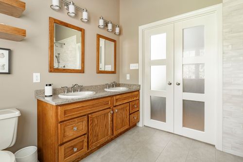 Oak double vanity with granite counter beside frosted glass double doors