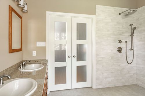 Bathroom double vanity with oak cabinets, granite counter and tiled walk-in shower beyond