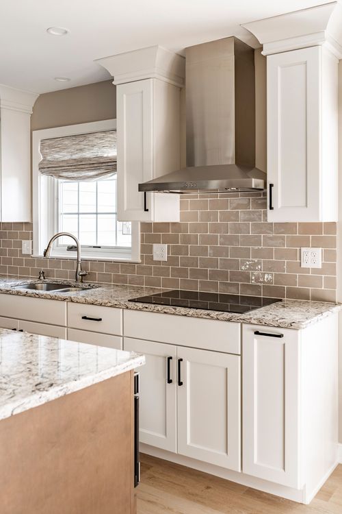 Kitchen with stainless range hood, subway tile backsplash and wood-toned island edge