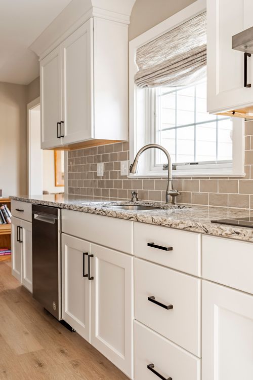 Kitchen with white cabinetry, granite counters, stainless dishwasher and a shaded window