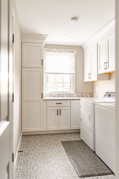 Laundry room with white cabinetry, patterned tile floor and white washer and dryer