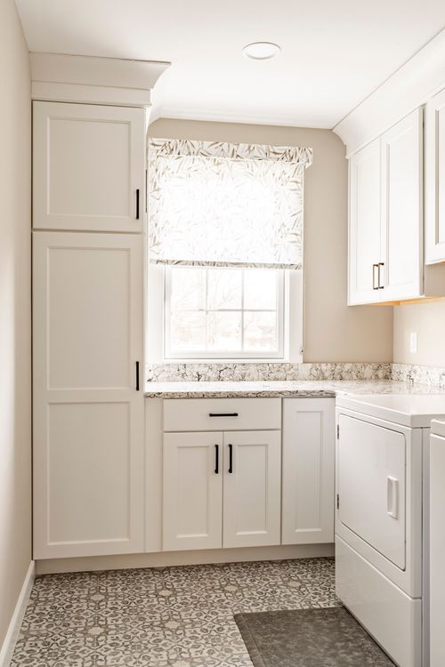 Laundry room with tall white pantry cabinets, granite counter and patterned tile floor