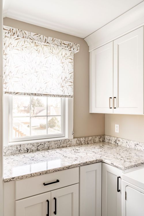 Corner kitchen counter with granite surface and a leaf-print roman shade window