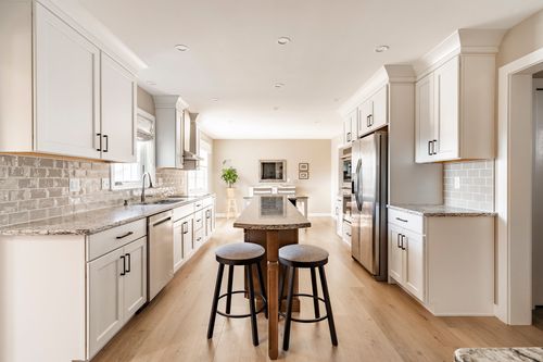 Open kitchen with white cabinets, round wood island table and dining area beyond