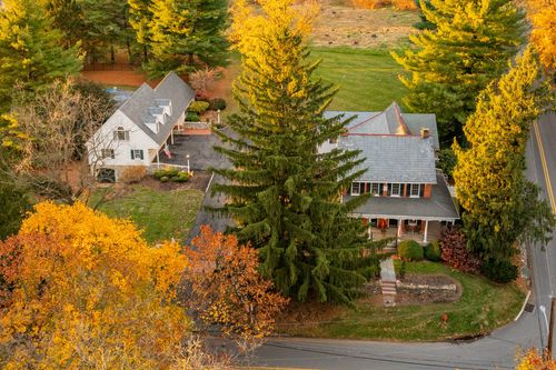 Aerial view of a brick farmhouse and matching carriage house surrounded by fall foliage