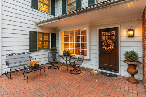 Brick patio with wrought iron furniture, potted mums and a wreathed front door