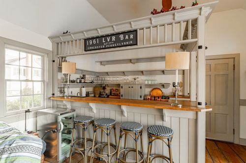 Built-in home bar with striped counter stools and a vintage lounge sign