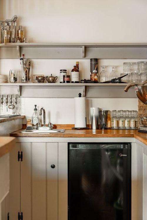 Kitchenette shelving with glassware over a wood counter and black mini fridge