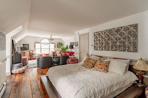 Bedroom with vaulted ceiling, tin-tile wall art and wood plank floors