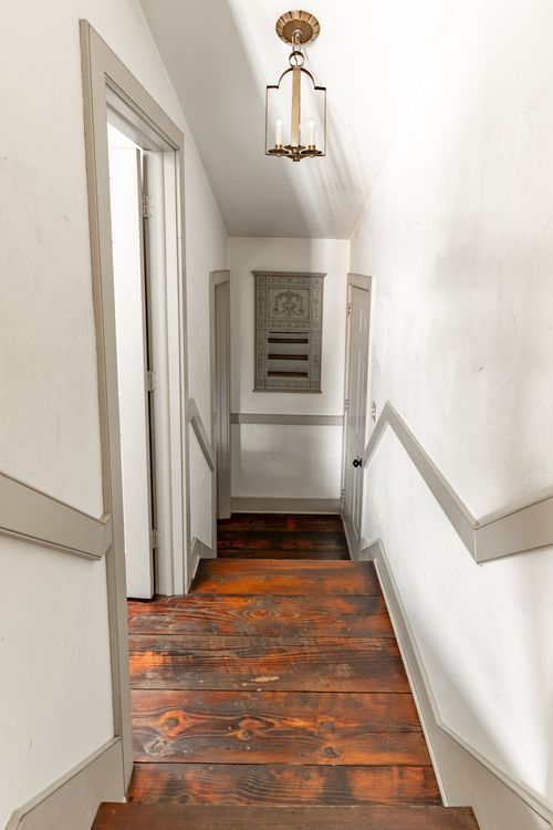 Narrow hallway with wood plank floors and a brass pendant light