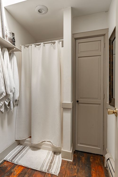 Bathroom nook with a shower curtain, hanging towels and a gray paneled door