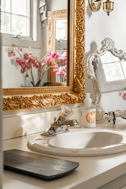 Close-up of a bathroom vanity with a gold mirror, pink orchids and chrome faucet