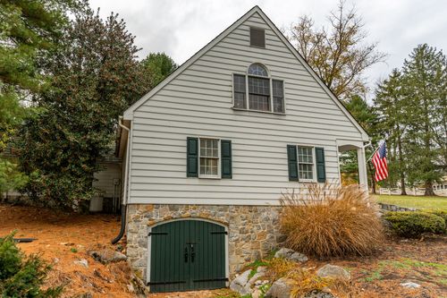 Stone and wood carriage house with green arched doors and an American flag