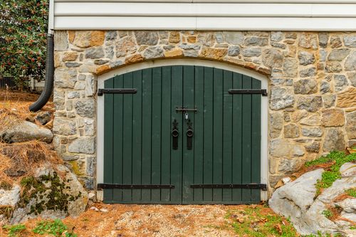 Close-up of a stone archway with dark green wood double doors and iron hardware