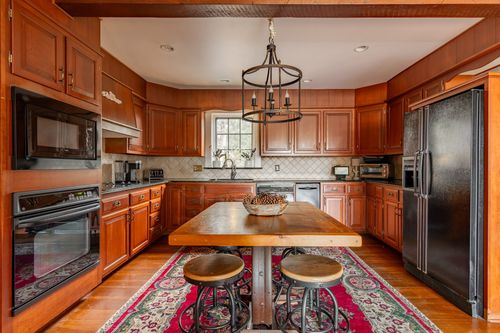 Kitchen with wood cabinetry, black appliances and a farm table beneath a chandelier