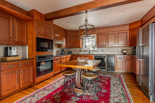 Kitchen with wood cabinetry, black appliances and a red patterned area rug