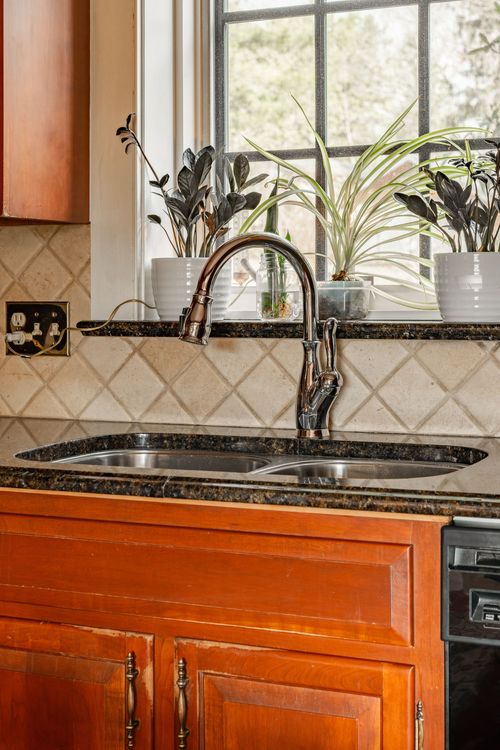 Kitchen sink with dark granite counter, tile backsplash and potted plants on the sill