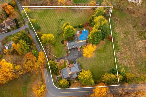 Aerial view of a fenced property with in-ground pool, farmhouse and expansive lawn