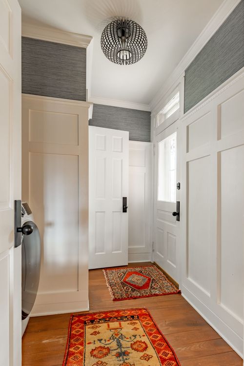 Entryway with textured gray wallpaper, black pendant light and layered oriental rugs