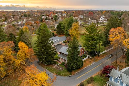 Aerial view of a brick farmhouse at dusk surrounded by mature pine trees and fall color
