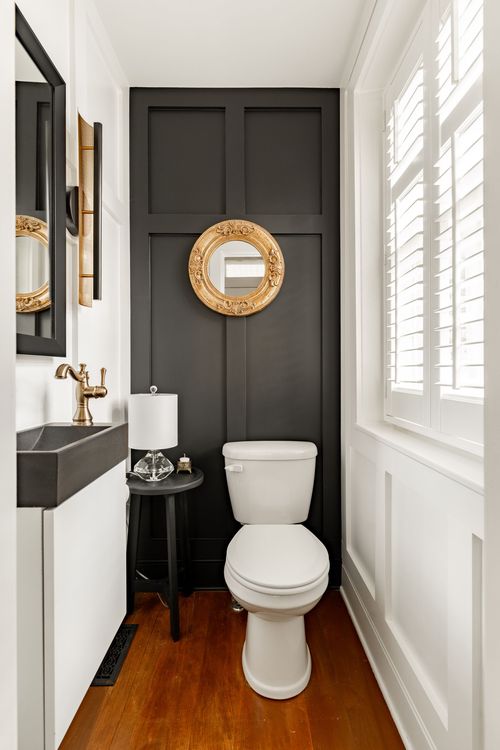Powder room with black board-and-batten wall, round gilt mirror and stone vessel sink