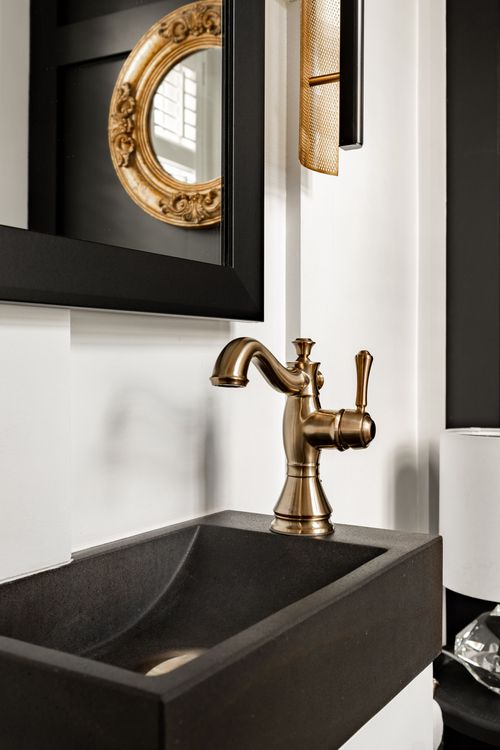 Close-up of a brass faucet and dark stone vessel sink beneath a gilt mirror