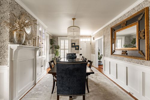 Dining room with floral wallpaper, gilt mirror, chandelier and a dark wood table