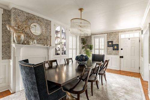 Dining room with patterned wallpaper, brass chandelier and black dining chairs