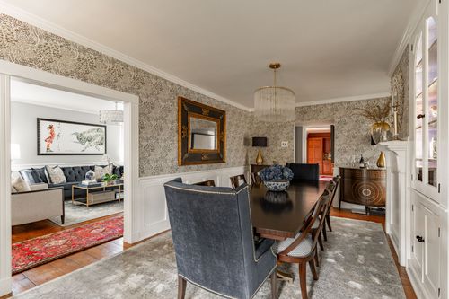 Dining room with patterned wallpaper opening to a living room with red oriental rug