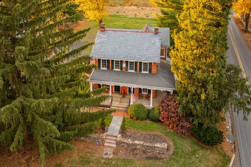 Aerial view of a brick colonial farmhouse with wraparound porch and autumn trees