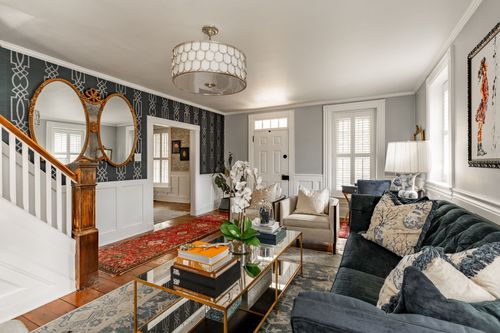 Living room with dark green tufted sofa, oval mirrors and a red runner rug near the stairs