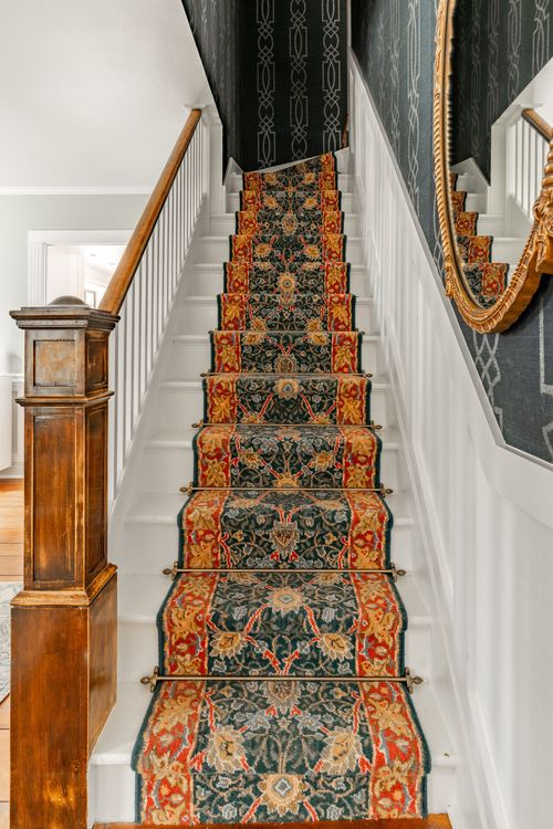 Staircase with a richly patterned runner rug and antique wood newel post
