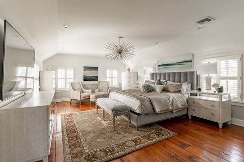 Primary bedroom with tufted gray headboard, starburst chandelier and sitting area