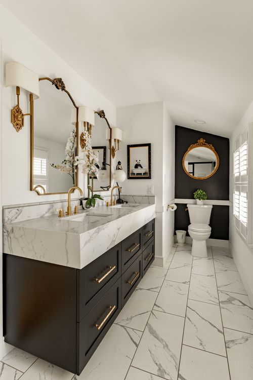 Bathroom with black double vanity, marble counter, gold fixtures and mirrored sconces