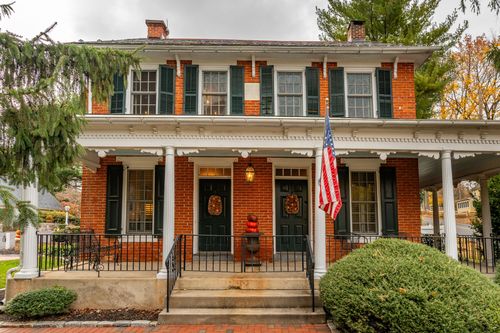 Brick farmhouse porch with black shutters, American flag and wreaths on double doors