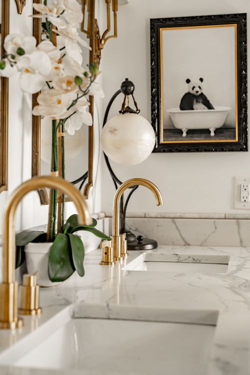 Close-up of gold faucets, marble counter, orchids and framed panda artwork