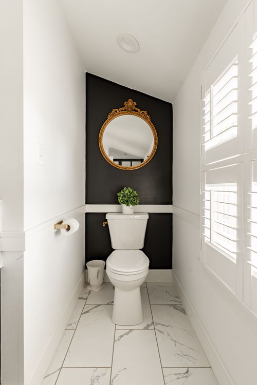 Small powder room with black accent wall, round gilt mirror and marble tile floor