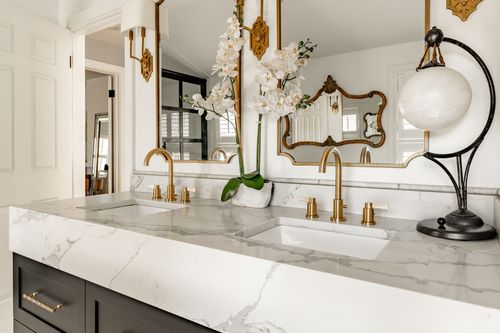 Close-up of a marble bathroom vanity with gold faucets, orchids and an ornate mirror