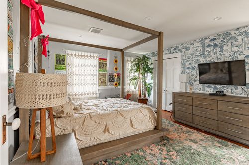 Bedroom with a wood canopy bed, botanical wallpaper accent wall and boho decor